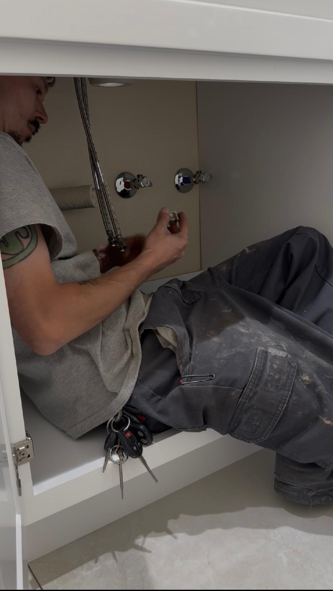Plumbing Repair Experts technician repairing bathroom faucet supply lines under white vanity cabinet in Las Vegas, NV