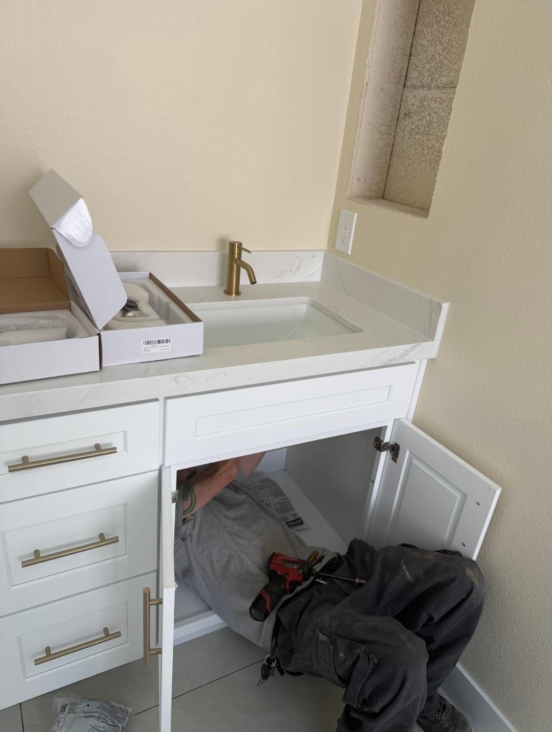 Plumbing Repair Experts technician connecting plumbing under white vanity with brushed gold faucet in Las Vegas, NV