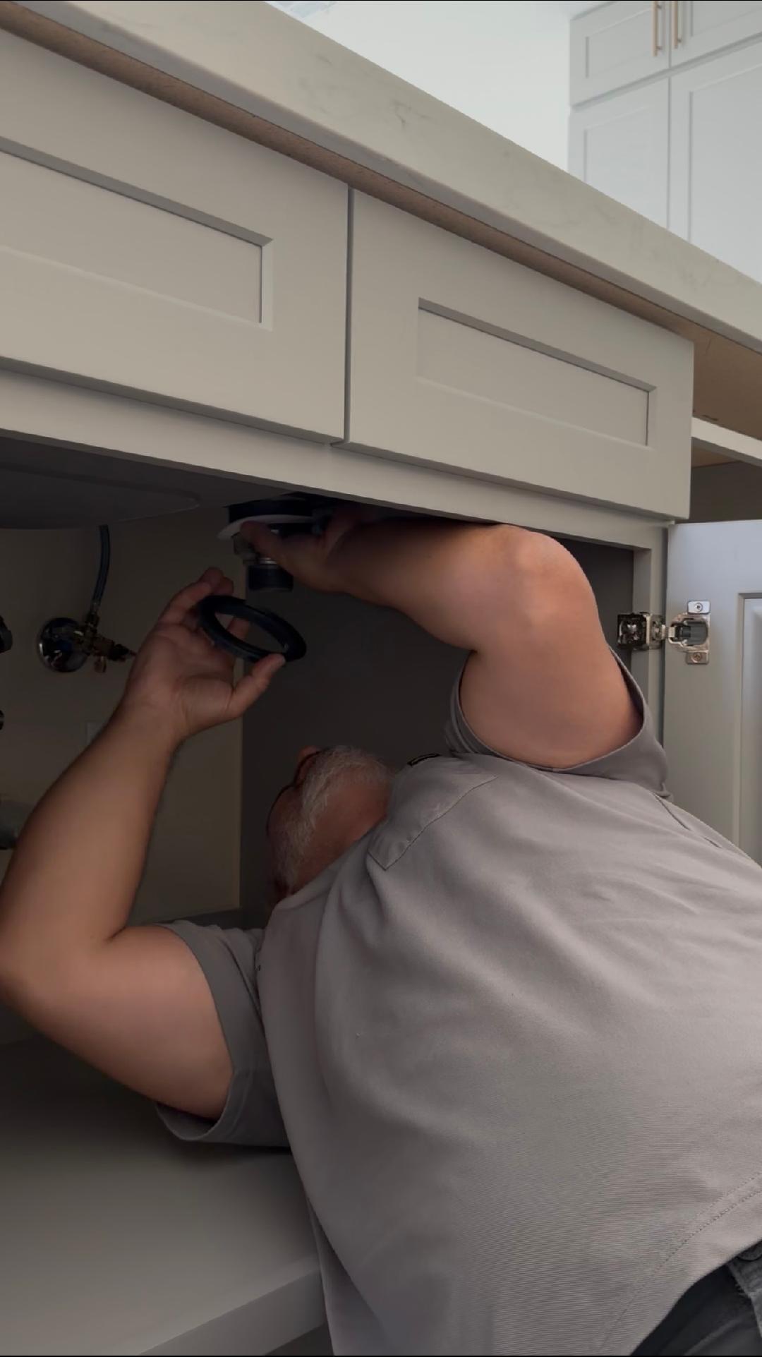 Plumbing Repair Experts plumber installing faucet drain assembly under kitchen sink cabinet in Las Vegas, NV